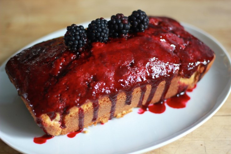 A picture of a cake with blackberry glaze and fresh blackberries